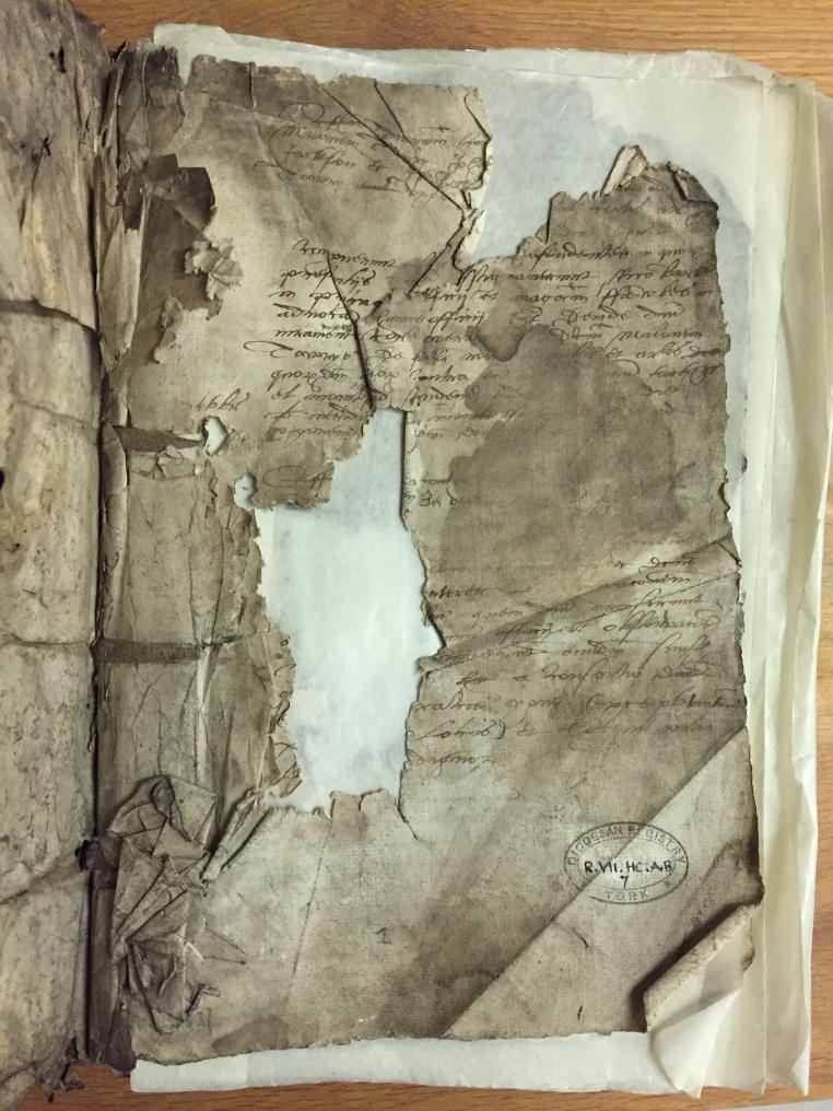 Damaged and dirty first page of a 16th century High Commission Act Book with a large loss in the middle and another at the top of the page.